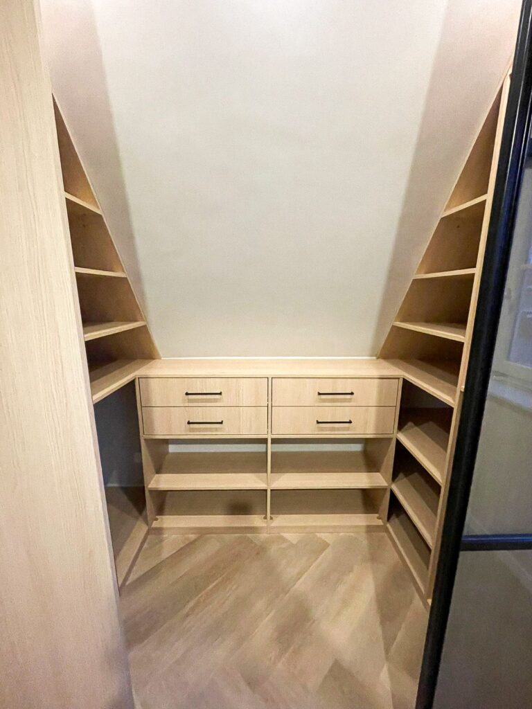 Compacte inloopkast onder een schuin plafond met ondiepe kasten en praktische indeling.